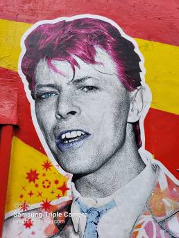 Street art of David Bowie with pink hair on red and yellow striped wall