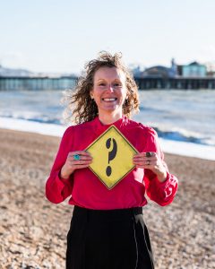Jo Murfin Career Coach Brighton holding a yellow question mark sign on Brighton beach